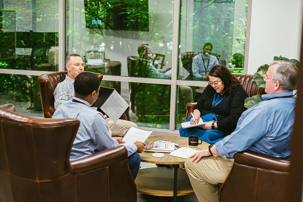 Four members of the Anesthesia Resources team sitting around a coffee table in their office talking and taking notes