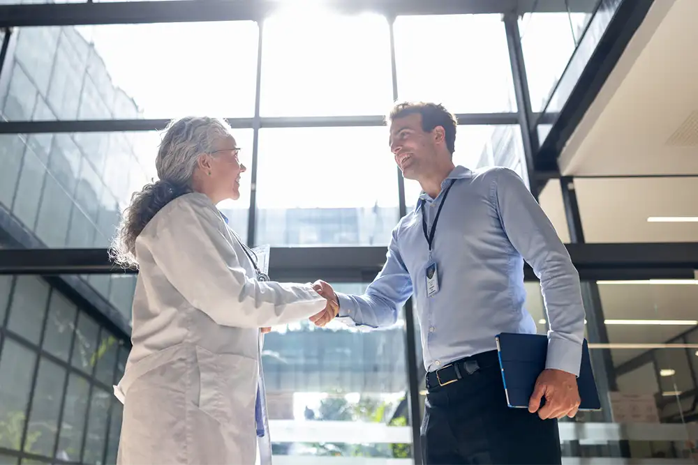 A businessman shaking hands with a physician in the entrance of a hospital