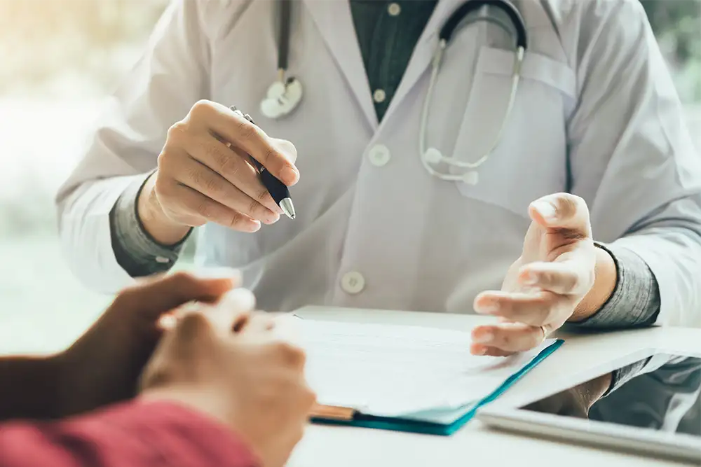 Close up image of a doctors holding a pen with a clipboard infront of him at a table