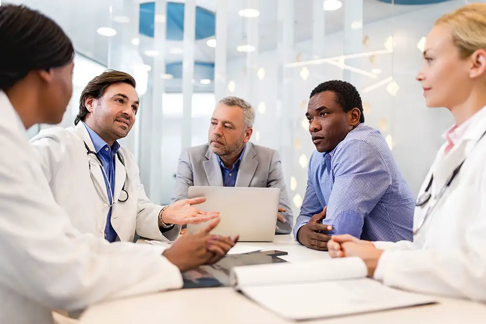 A group of doctors and business people sitting at a table talking in a bright white room