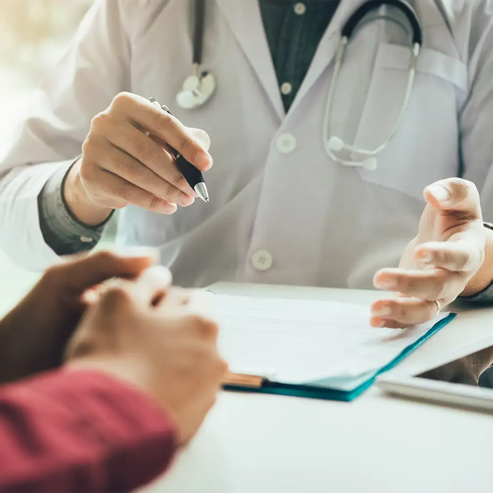 Close up image of a doctors holding a pen with a clipboard infront of him at a table