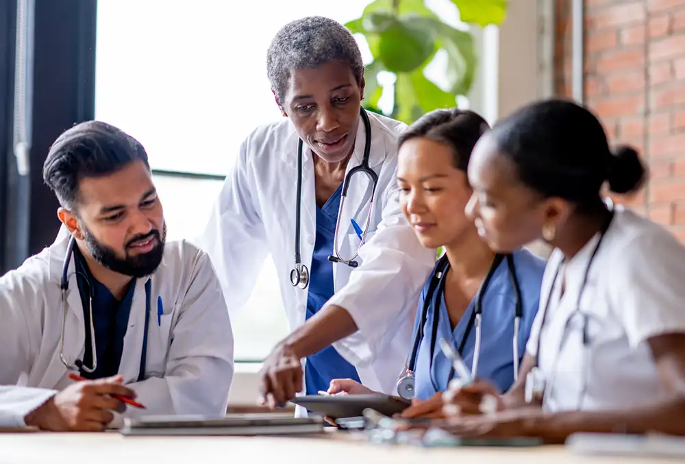 Four physicians sitting around a table looking at tablets and paperwork