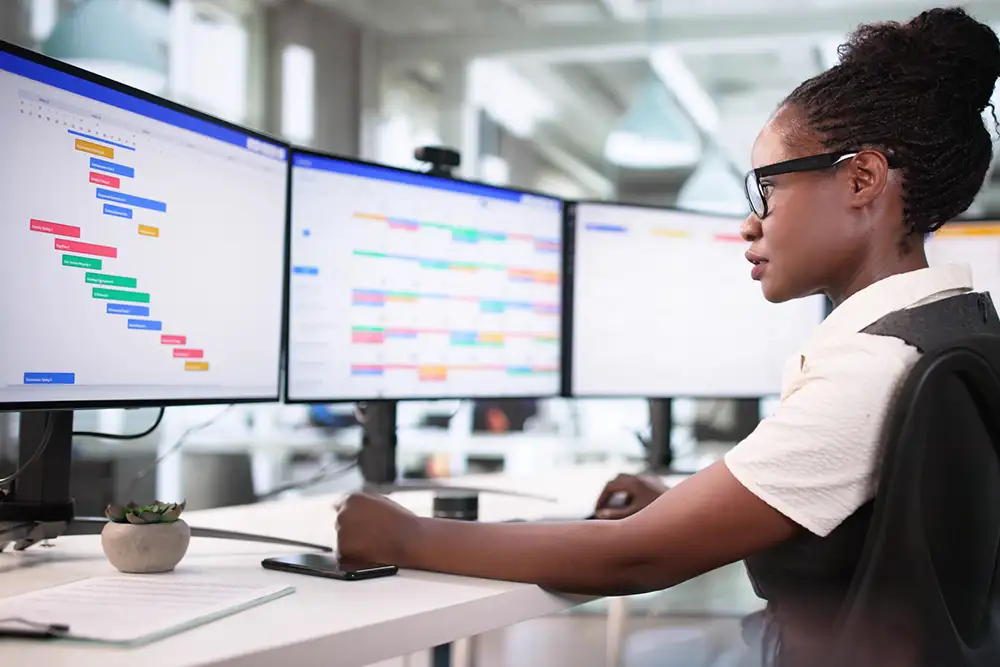 A businesswoman sitting infront of a few computer screens with graphs and charts on them