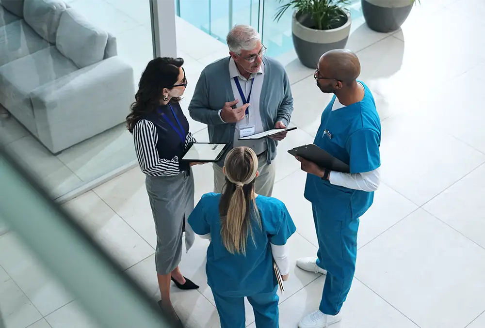 Two physicians and two business people standing in a hospital hallway holding tablets and talking