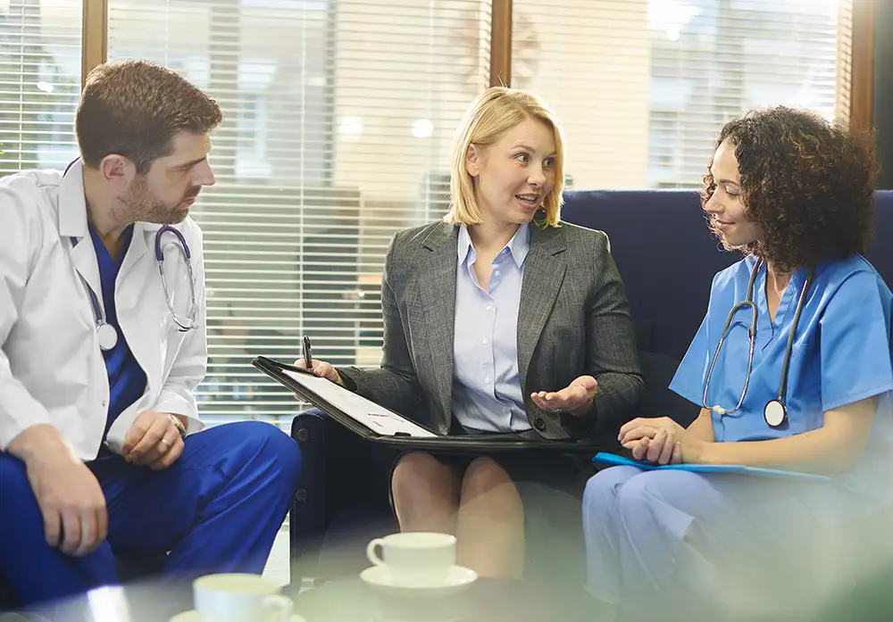 A businesswoman sitting on a couch with a portfolio talking to two physicians